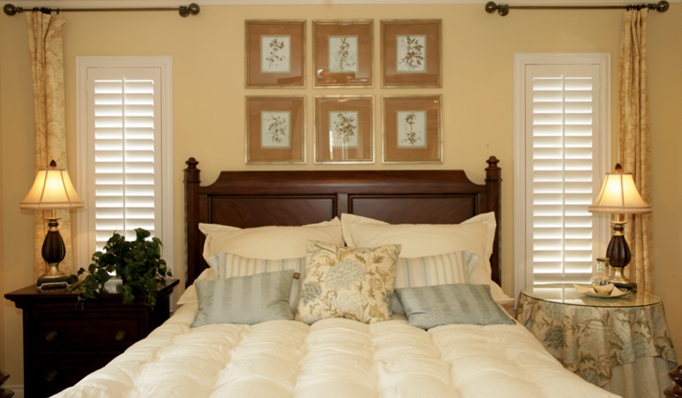 Tall plantation shutters framing bed in a bedroom in Sacramento 